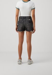 Czarne krótkie spodenki jeansowe z postrzępionymi krawędziami i standardowymi tylnymi kieszeniami, połączone z białym t-shirtem z zielonymi akcentami oraz sportowymi butami.