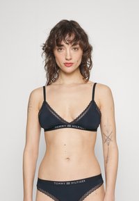 Bralette musta lace-trimmed ja säädettävillä olkaimilla, joka on varustettu brändillä varustetulla vyötärönauhalla, yhdistettynä vastaaviin mustiin alushousuihin. Pehmeä kangas saumattomalla designilla.