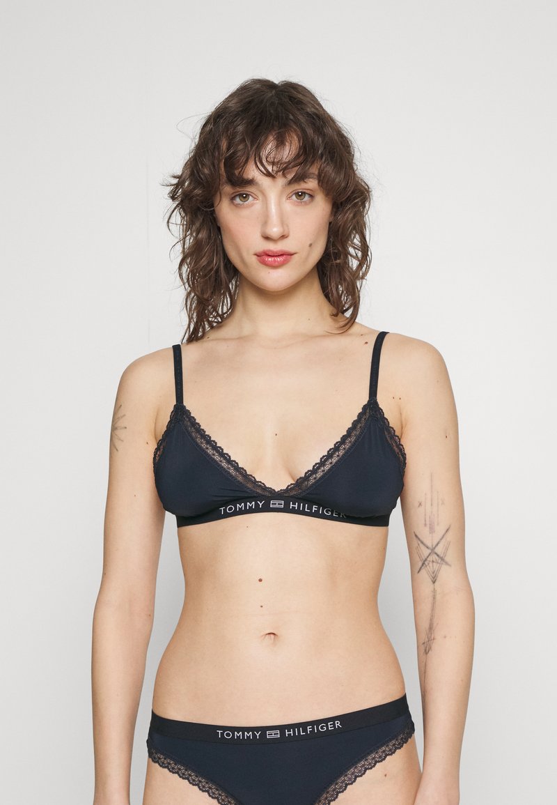 Bralette musta lace-trimmed ja säädettävillä olkaimilla, joka on varustettu brändillä varustetulla vyötärönauhalla, yhdistettynä vastaaviin mustiin alushousuihin. Pehmeä kangas saumattomalla designilla.