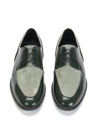 Een paar donker groene leren en grijze suède herenschoenen met veters, van bovenaf weergegeven op een witte achtergrond.