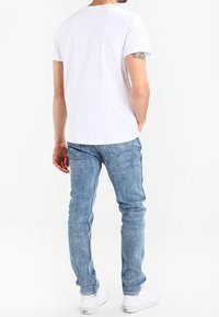 Vitt bomullströja i kombination med ljusblå denimjeans. Jeansarna har en slim fit och är designade med bakfickor. Vita sneakers fulländar looken.