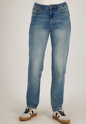 Lichtblauwe mid-rise jeans met subtiele vervaagde details, rechte pasvorm, gedragen met witte sneakers met zwarte strepen en gumzolen.