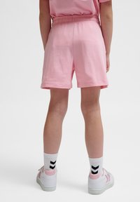 Shorts en coton rose avec une taille élastique, présentant une coupe décontractée. Portés avec des baskets blanches et des chaussettes blanches à motif chevron noir.