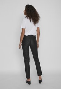 Pantalones negros de cintura alta con corte ajustado, bolsillos traseros y textura suave, combinados con una camiseta blanca básica y tacones negros.