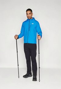 Μπλε ελαφρύ μπουφάν με κουκούλα, μαύρο παντελόνι και μπαστούνια πεζοπορίας. Το μπουφάν διαθέτει τσέπη με φερμουάρ και εφαρμοστά μανίκια. Μαύρα παπούτσια ολοκληρώνουν την εμφάνιση.