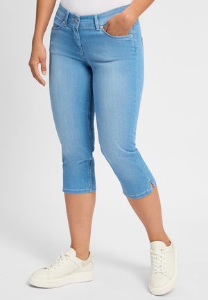 Lichtblauwe cropped jeans gemaakt van denim. Heeft voorzakken, zichtbare stiksels en zijsplitten aan de zoom. Gekozen met witte sneakers.