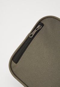 Pliculeț din material verde cu o textură netedă, având un fermoar negru pe margine și colțuri rotunjite pentru un design compact.
