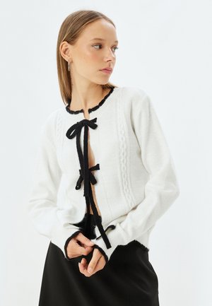 Witte cardigan met zwarte accenten, met een ribbelstructuur, kabelbrei-details en strikjes aan de voorkant; lange mouwen en slim fit.