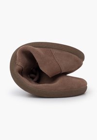 Brown suede slipper with a soft texture, rounded shape, and flexible sole, showing the interior and an elastic closure detail.