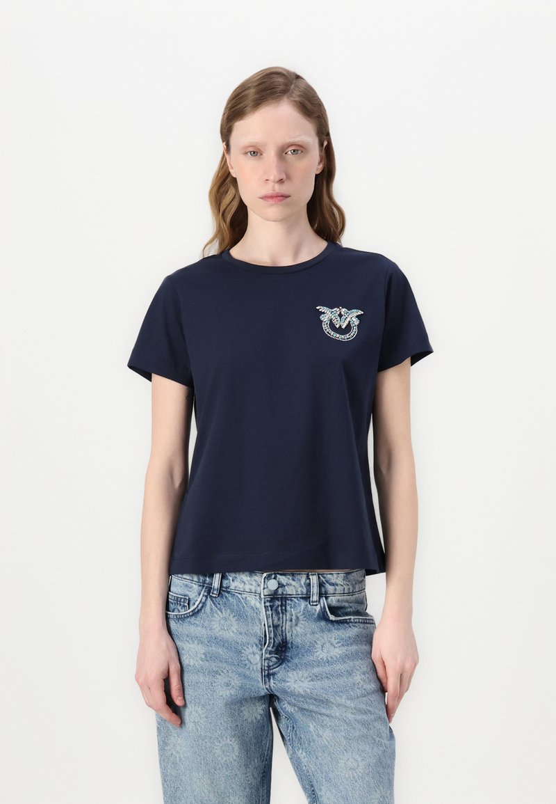 T-shirt di cotone blu navy con collo rotondo, maniche corte e un motivo ricamato decorativo sul lato sinistro del petto. Abbinato a jeans azzurri.