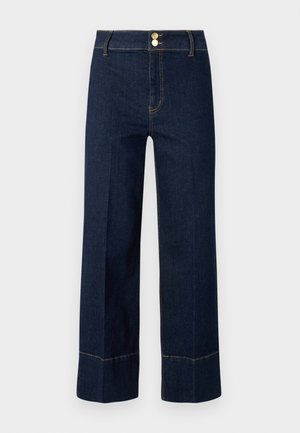 Mørkeblå høyt liv vide jeans med doble gullknapper og synlig oransjefarging på en lys bakgrunn.