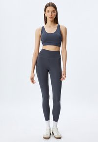 Grå atletisk cropped top og højtaljede leggings lavet af strækbar, glat stof. Har en tætsiddende design og flade sømme. Fodtøj: beige sneakers.