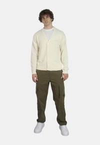 Cardigan in cotone crema con scollo a V e bottoni, abbinato a pantaloni cargo oliva con tasche con zip e sneakers bianche.