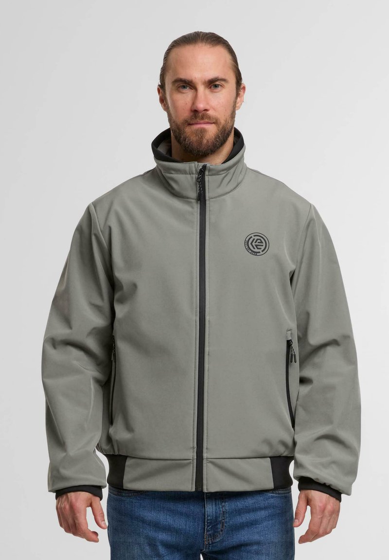 Grau weiche Schale Jacke mit hohem Kragen, schwarzen Akzenten, seitlichen Reißverschlusstaschen und einem Logo auf der linken Brust. Besitzt einen glatten, strukturierten Stoff.