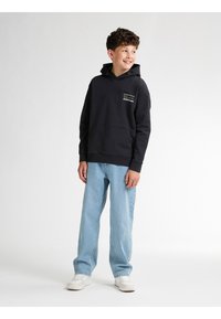 Felpa nera con cappuccio, dotata di tasca frontale e dettaglio del logo, abbinata a jeans blu chiaro a gamba larga e sneakers bianche.
