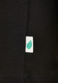 Svart stoff med en subtil ribbestruktur, med et hvitt merke med et grønt blad-design på kanten, som indikerer bærekraftig merking.