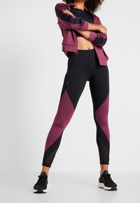 Sportleggings in Schwarz mit Pflaumenfarbenen Einsätzen, mit hoher Taille und glatter Textur. Kombiniert mit einer passenden Zip-Jacke.