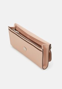 Růžová kabelka na ruku s hladkým povrchem, vybavená stříbrným zapínáním na knoflík a jednou otevřenou přihrádkou. Okraje jsou lemovány tmavě hnědou barvou.