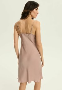 Kobieta w bezrękawnikowej, jasnofioletowej sukience na ramiączkach z cienkimi, regulowanymi paskami, pokazana z tyłu na jasnym, jednolitym tle.