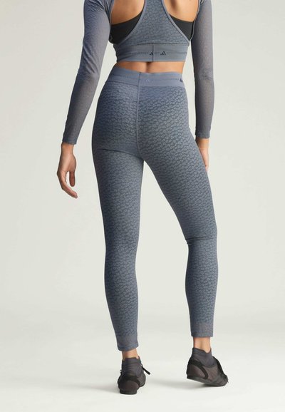 Blue textured leggings with a fitted design, featuring a patterned surface and high waistband. Black athletic shoes complement the outfit.