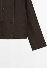 Mörkbrun långärmad jacka med dubbelknäppt knappfront och fransade kanter vid ärm och fåll.