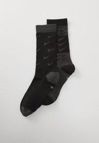 Dva para Nike nogavic: en par v enotni črni barvi, drugi temno sivi z svetlo sivo potiskano ikono Nike. Z ribastimi robovi, mehka tekstura, dolžina do gležnja.