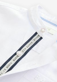 Witte blouse met marineblauwe gestreepte binnenvoering. Voorzien van merkknopen en geborduurd logo bij de halslijn. Glad textuur.