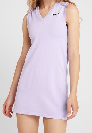 Robe Nike sans manches violet clair avec col en V portée par une personne aux longs cheveux, montrée du cou à mi-cuisse sur un fond uni.
