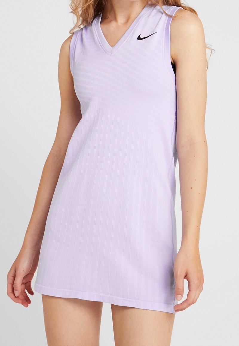 Robe Nike sans manches violet clair avec col en V portée par une personne aux longs cheveux, montrée du cou à mi-cuisse sur un fond uni.
