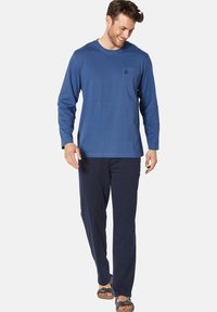 Long-sleeve blue shirt with crew neckline and a chest pocket, paired with dark blue pants and sandals, featuring a relaxed fit.
