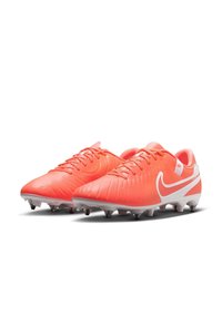 Nike jalgpallijalatsid erksas korallis valgete aktsentidega; tekstuuriga sünteetiline pealmine osa, paelkinnitus ja strateegiliselt paigutatud nupud valgel tallal.