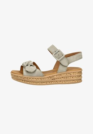 Beige kile sandal med tekstureret korksål, ankelrem med spænde og frontrem med dekorativ blomst detalje.