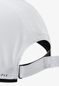 Gorra blanca de tejido ligero, con visera curva, detalles cosidos y una correa ajustable en la parte trasera. El texto muestra el nombre de la marca.