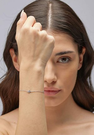 Braccialetto d'argento con charm a forma di stella, design della catena delicato e finitura lucida, indossato su un polso con una carnagione chiara.