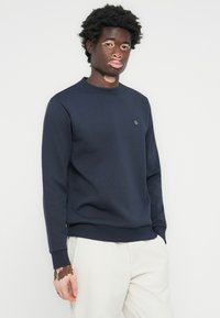 Mørkeblå hettegenser med rund hals, ribbestrikkede cuffs og kant, med en liten logo på brystet og et mykt, strukturert stoff.