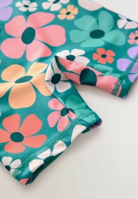 Kleurige zwembroek van tealen stof met grote roze, witte en groene bloemmotieven, met een gladde textuur en een elastische tailleband.