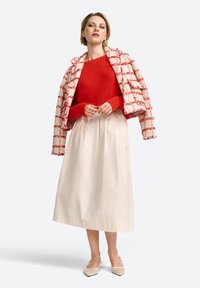 Un pull à côtes rouges associé à une jupe blanche, complété par une veste en tweed à carreaux rouges et blancs. Les accessoires incluent des chaussures à talons beiges.