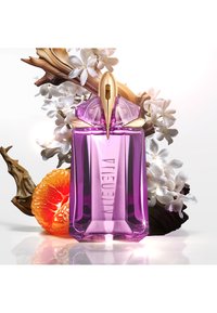 Paarse glazen parfumfles met een geometrisch ontwerp. Gouden accenten aan de bovenkant, omringd door witte bloemen en een feloranje vrucht.
