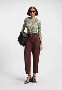 Long-sleeve, floral-patterned top in green and yellow, paired with high-waisted maroon trousers. Black structured handbag and black strappy heels.