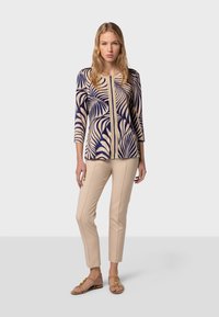 Top ajusté à manches longues avec un motif de feuilles de palmier bleu marine et beige. Associé à un pantalon slim beige et des sandales beiges.