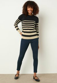 Schwarz-beige gestreifter Pullover mit langen Ärmeln, Rundhals-Ausschnitt, taillierter Passform. Trägt man mit dunkelblauen Skinny Jeans und schwarzen Ballerinas.
