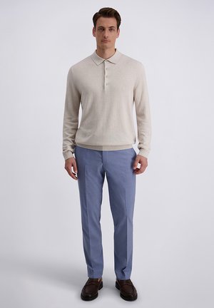 Beige Strick-Poloshirt mit Kragen und drei Knöpfen, kombiniert mit hellblauen, maßgeschneiderten Hosen und dunkelbraunen Loafers. Einfaches und modernes Design.