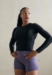 Sort langærmet atletisk top med mesh-sidelapper, parret med lilla tætsiddende shorts. Glat, strækbart stof med en slank silhuet.