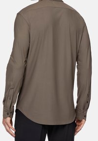 Camicia a maniche lunghe color kaki scuro con orlo curvo, polsini con bottoni e tessuto morbido e leggero. La vista posteriore mostra una vestibilità su misura e cuciture sulle spalle.