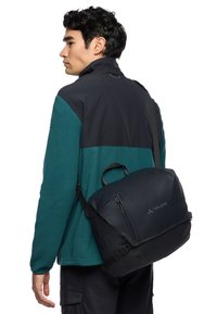 Bolsa Vaude negra con superficie texturizada, compartimentos con cremallera y correa ajustable. El material es duradero, diseñado para la funcionalidad y el estilo.