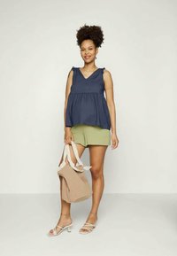 Top sem mangas azul-marinho com decote em V e acentos de laço, combinado com calções verdes-oliva e uma mala tote bege; sandálias brancas com tiras.