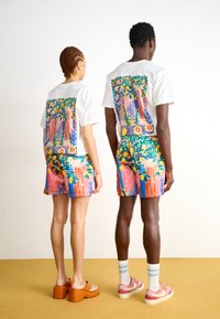 Hvide t-shirts med farverige rygprint og matchende livlige shorts med blomster- og geometriske mønstre. Modellerne har orange platform sko på.