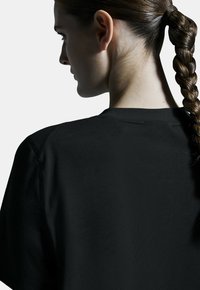 Schwarzes kurzärmliges Oberteil mit Rundhalsausschnitt. Glatte Textur, mit kontrastierenden Nähten entlang der Schulternaht und einer lockeren Passform.