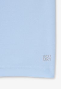 Tissu bleu clair avec un tissage texturé, comportant une petite étiquette embossée "ULTRA DRY" à l'ourlet, mettant en avant un design épuré et simple.