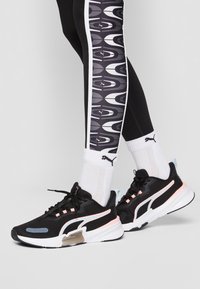 Svarta sportskor med rosa accenter, meshtopp och gummisula. Matchas med mönstrade svarta leggings och vita strumpor med en logotyp.